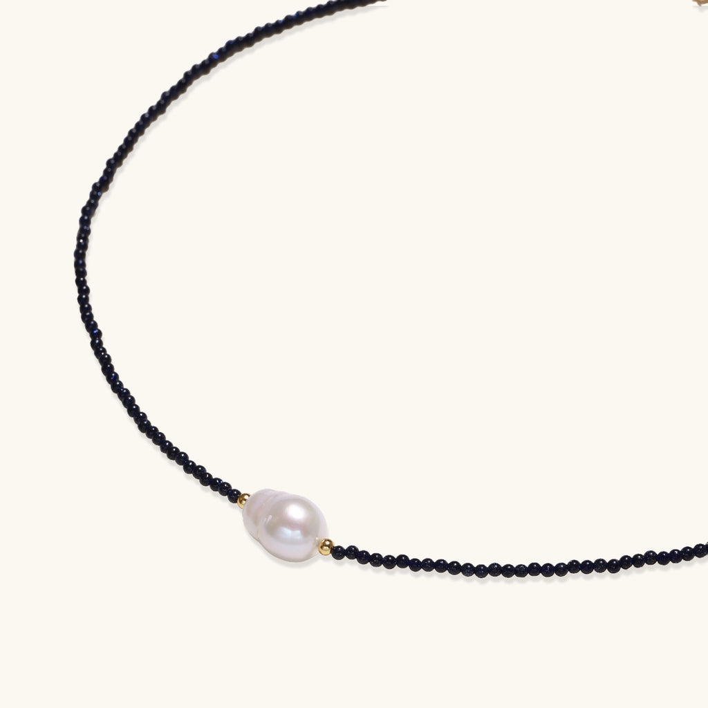 Elegant necklace with blue sandstone beads and baroque pearl centerpiece with gold accents on neutral background.