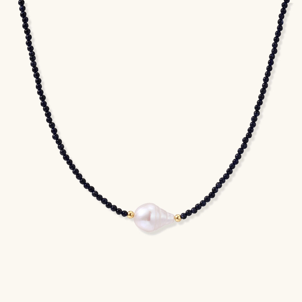 Elegant necklace with blue sandstone beads and baroque pearl centerpiece with gold accents on neutral background.