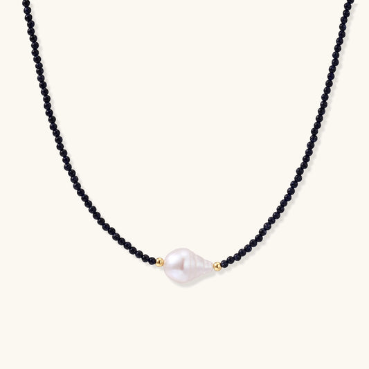 Elegant necklace with blue sandstone beads and baroque pearl centerpiece with gold accents on neutral background.