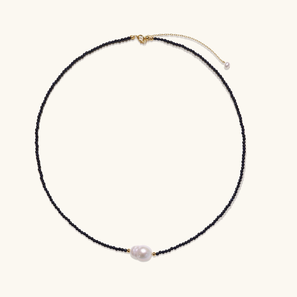 Elegant necklace with blue sandstone beads and baroque pearl centerpiece with gold accents on neutral background.