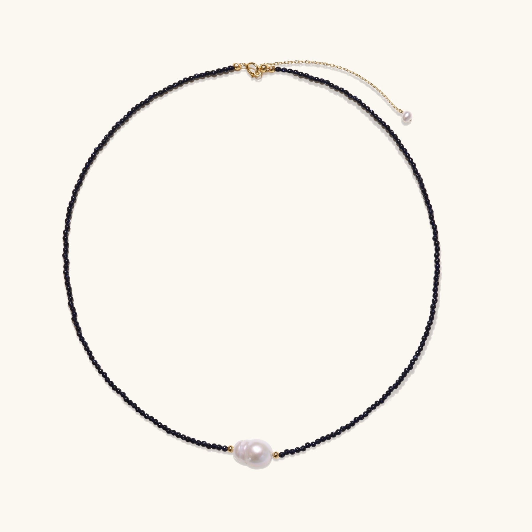 Elegant necklace with blue sandstone beads and baroque pearl centerpiece with gold accents on neutral background.