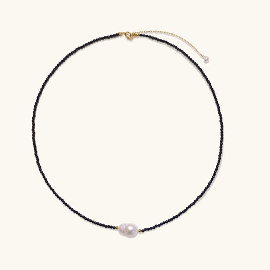 Elegant necklace with blue sandstone beads and baroque pearl centerpiece with gold accents on neutral background.