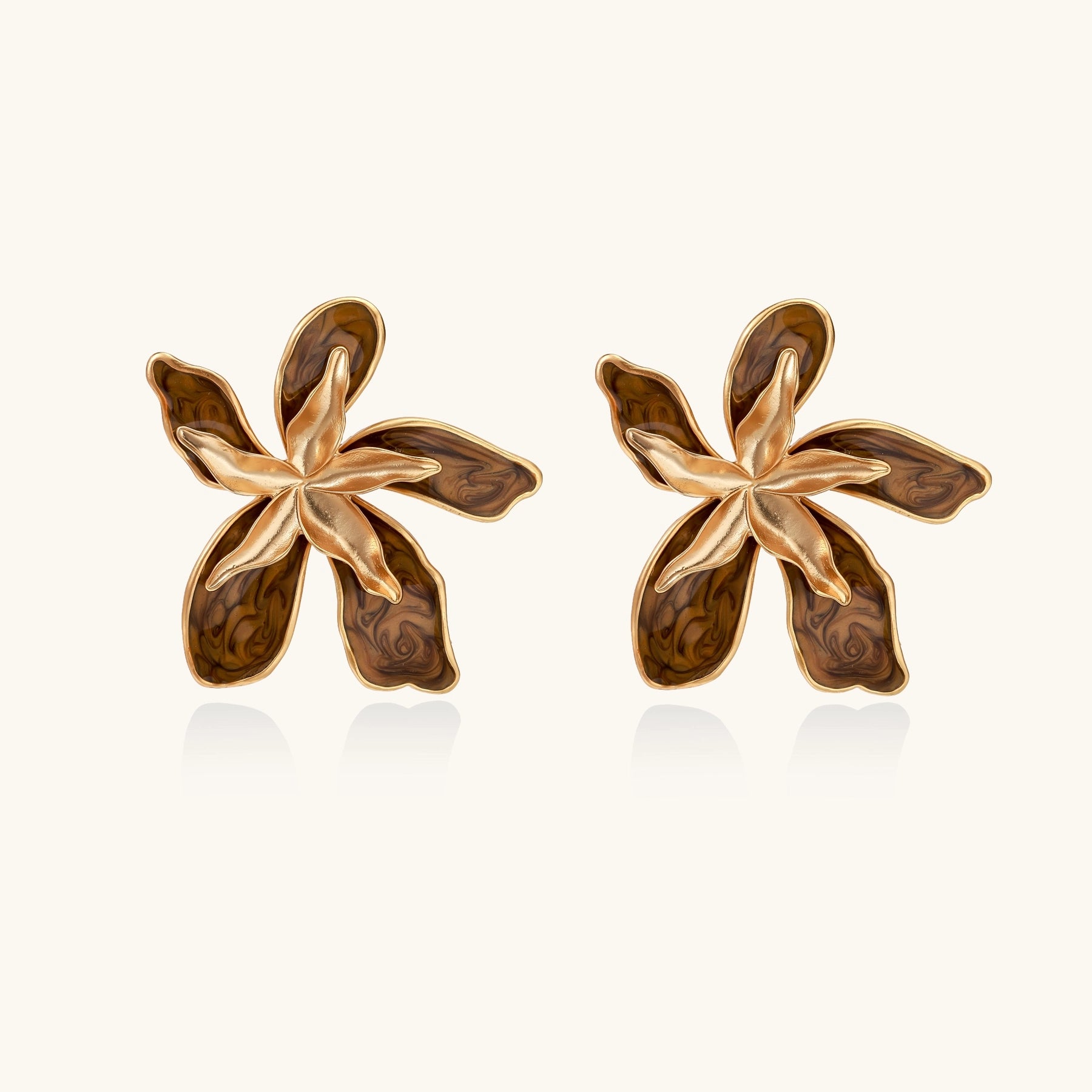 Large gold-plated flower earrings with brown enamel marbled petals on beige background, showing intricate floral design.