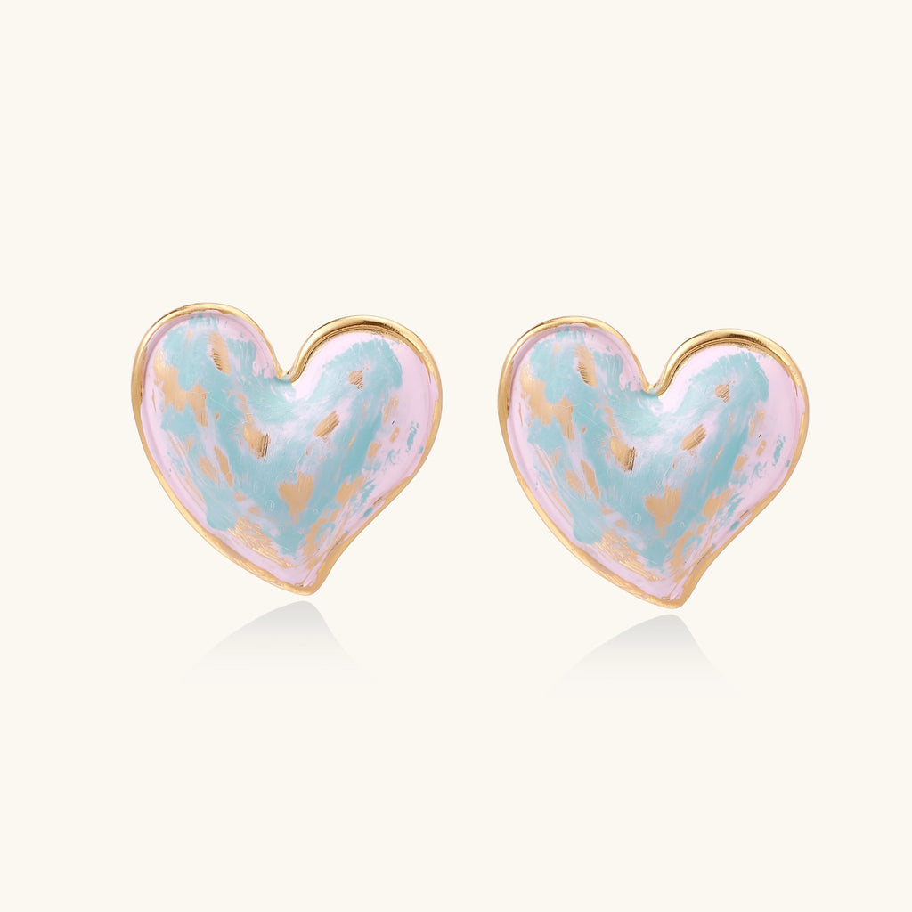 Heart-shaped stud earrings with iridescent blue-pink enamel finish and gold-plated brass frames against cream background
