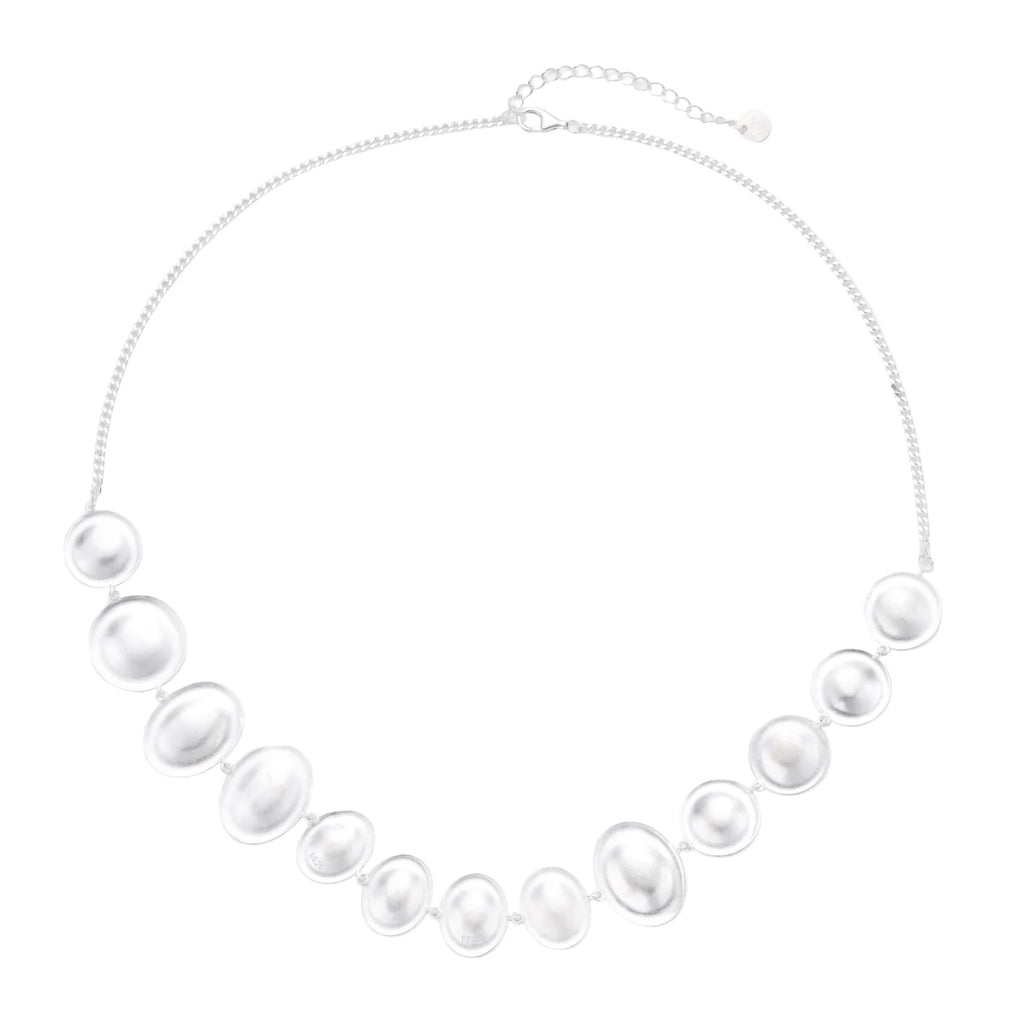 Graduated pearl-finish silver discs forming an organic bubble bib necklace on delicate chain against cream background.